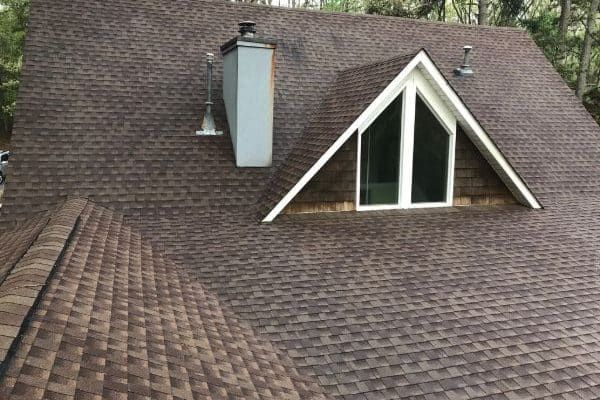 Brown shingle roof with a dormer window and chimney. Professional roof cleaning helps maintain the integrity and appearance of roofs like this one.